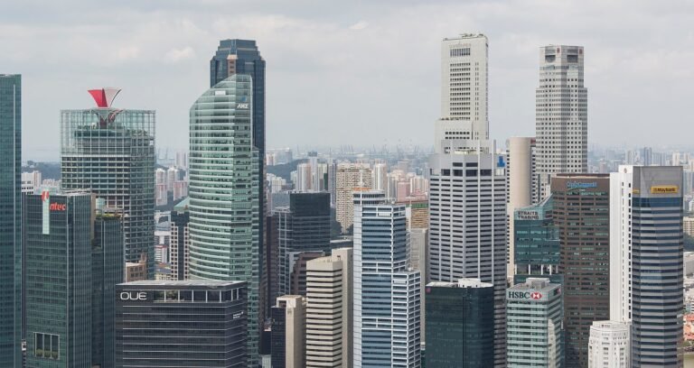 Singapore's Central Business District skyline at Marina Bay, featuring a dense cluster of high-rise commercial and financial towers including buildings bearing the ANZ, HSBC, OUE, NTUC, Straits Trading and Maybank signs, viewed from the Marina Bay Sands Hotel observation deck under a partly cloudy s