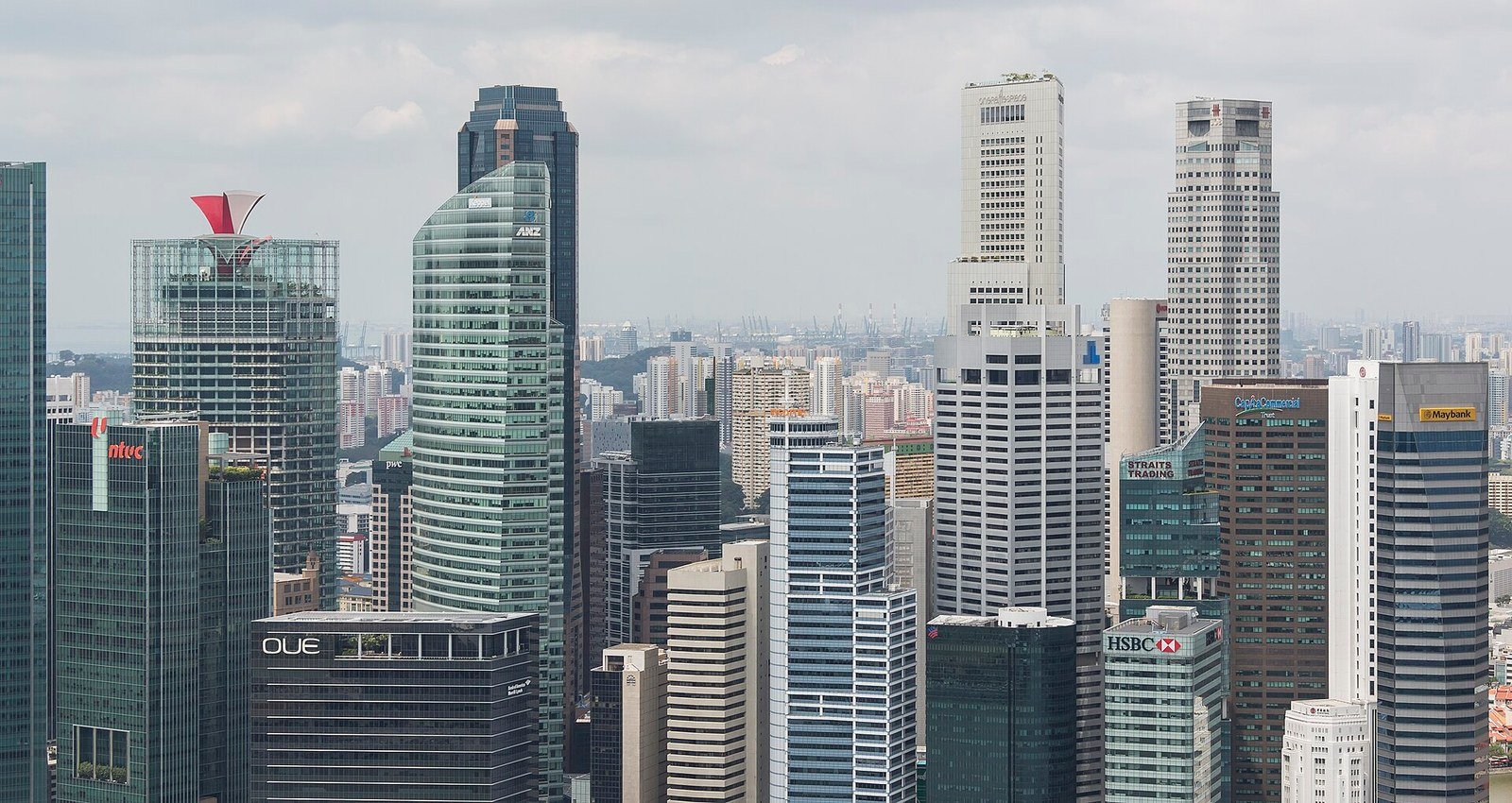 Singapore's Central Business District skyline at Marina Bay, featuring a dense cluster of high-rise commercial and financial towers including buildings bearing the ANZ, HSBC, OUE, NTUC, Straits Trading and Maybank signs, viewed from the Marina Bay Sands Hotel observation deck under a partly cloudy s